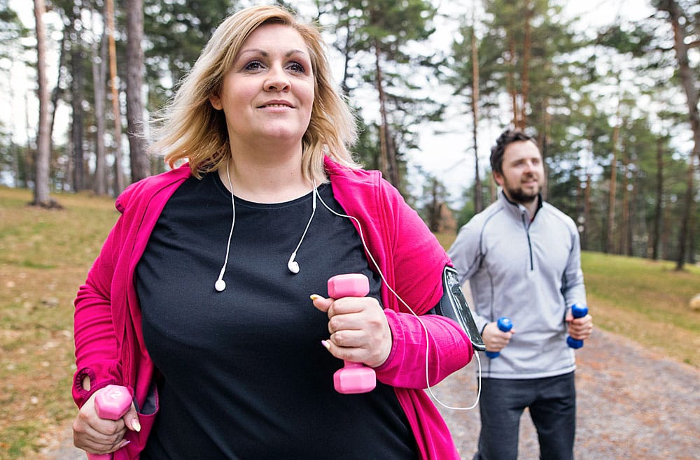 Woman exercising outside with pink weights in her hands